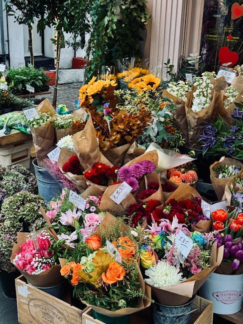 A vibrant display of fresh flowers arranged in various bouquets on a shop stand, featuring a mix of colorful blooms such as pink lilies, orange roses, white chrysanthemums, purple tulips, and red carn